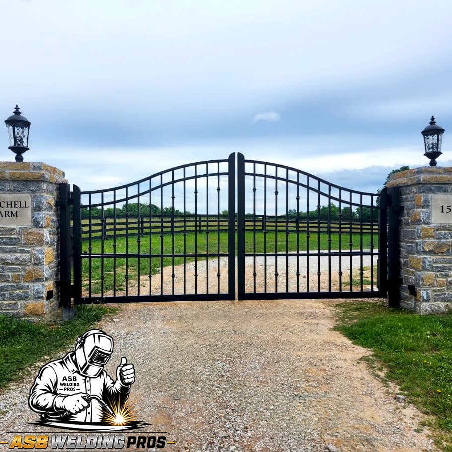 Arched black driveway gate installed between stone entrance columns.