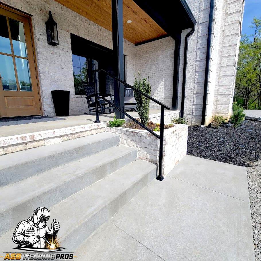 Black metal handrail installed beside concrete steps at a modern entry.