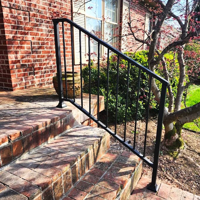 Black metal handrail following brick garden steps beside a home.