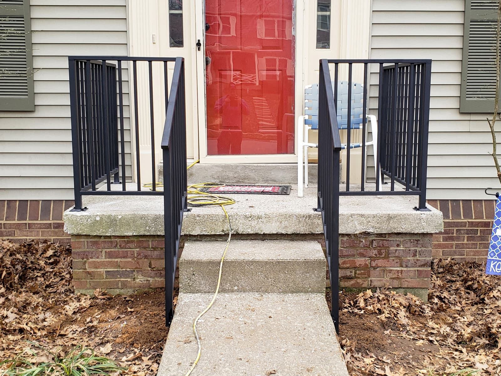 Black metal entry railing installed on concrete porch steps.